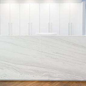 Moderner Empfangstresen aus weißem Marmor mit Schränken in heller, minimalistischer Praxis.