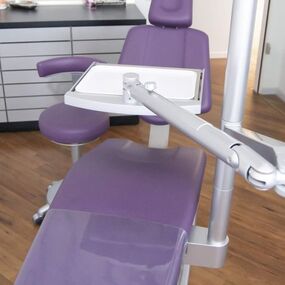 Lila Zahnarztstuhl mit moderner Behandlungseinheit in einer hellen Zahnarztpraxis.